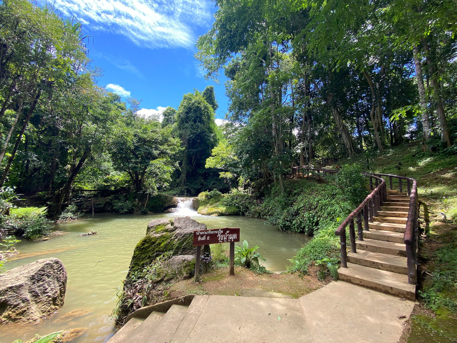 Steps down to a stream by a waterfall with a sign in Thai