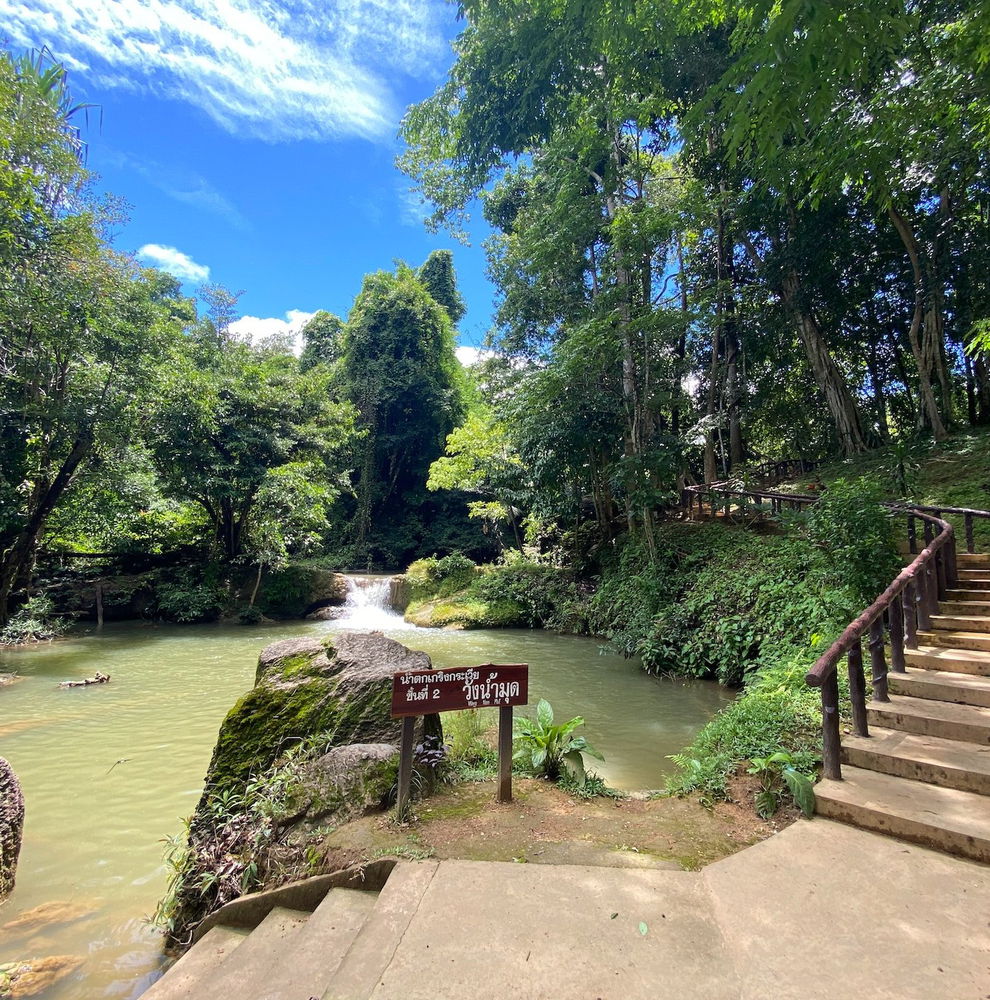 Steps down to a stream by a waterfall with a sign in Thai